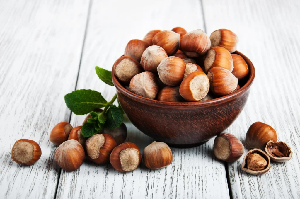 Un bol en bois rempli de noisettes avec quelques noisettes éparpillées.