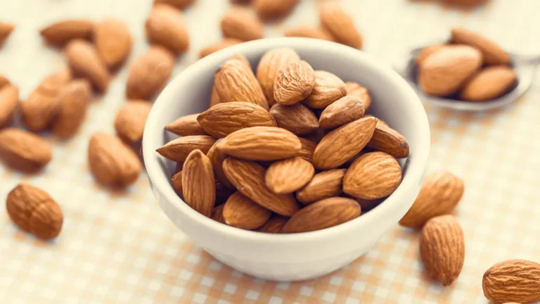 Amandes bienfaits: Un bol blanc rempli d'amandes avec des amandes éparpillées autour.