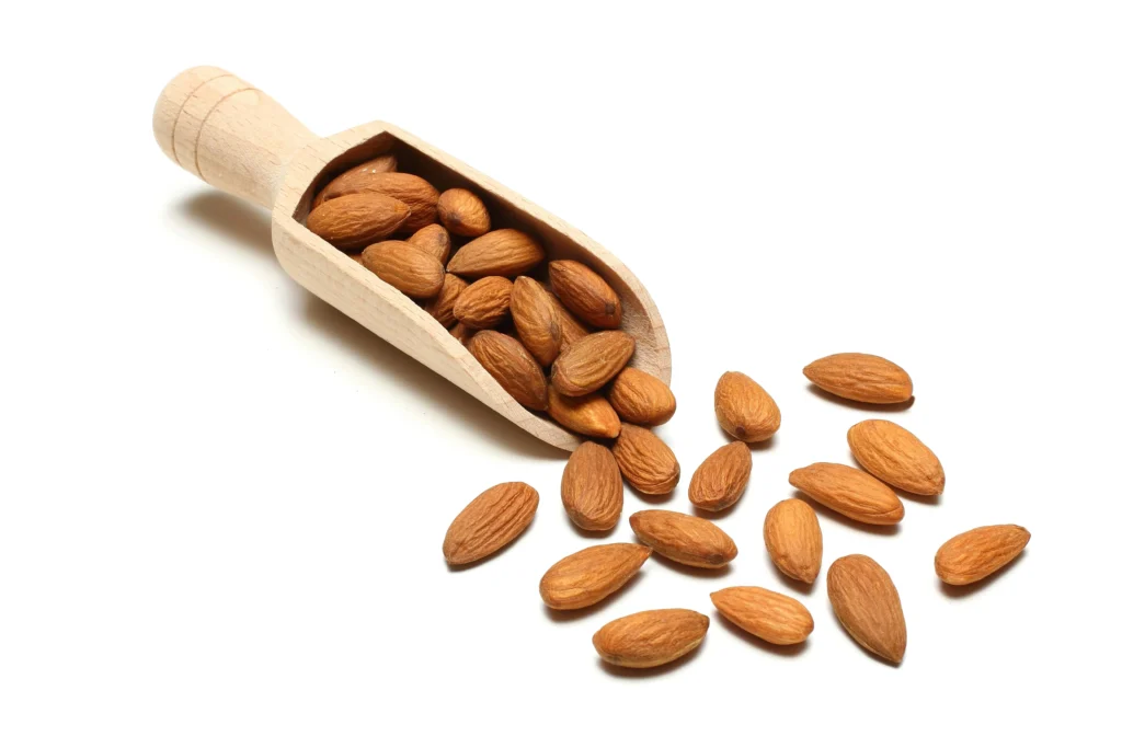 Amandes et perte de poids: Amandes dispersées avec une pelle en bois remplie d'amandes sur fond blanc.