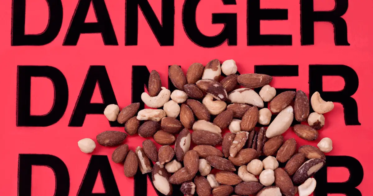 Alerte allergie-attention aux fruits à coque Mélange de fruits à coque posé sur un fond rouge avec le mot "DANGER" écrit en noir, illustrant le risque d’allergie alimentaire.